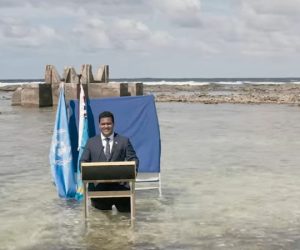 Photo of Hon Minister Simon Kofe standing in ocean with a podium